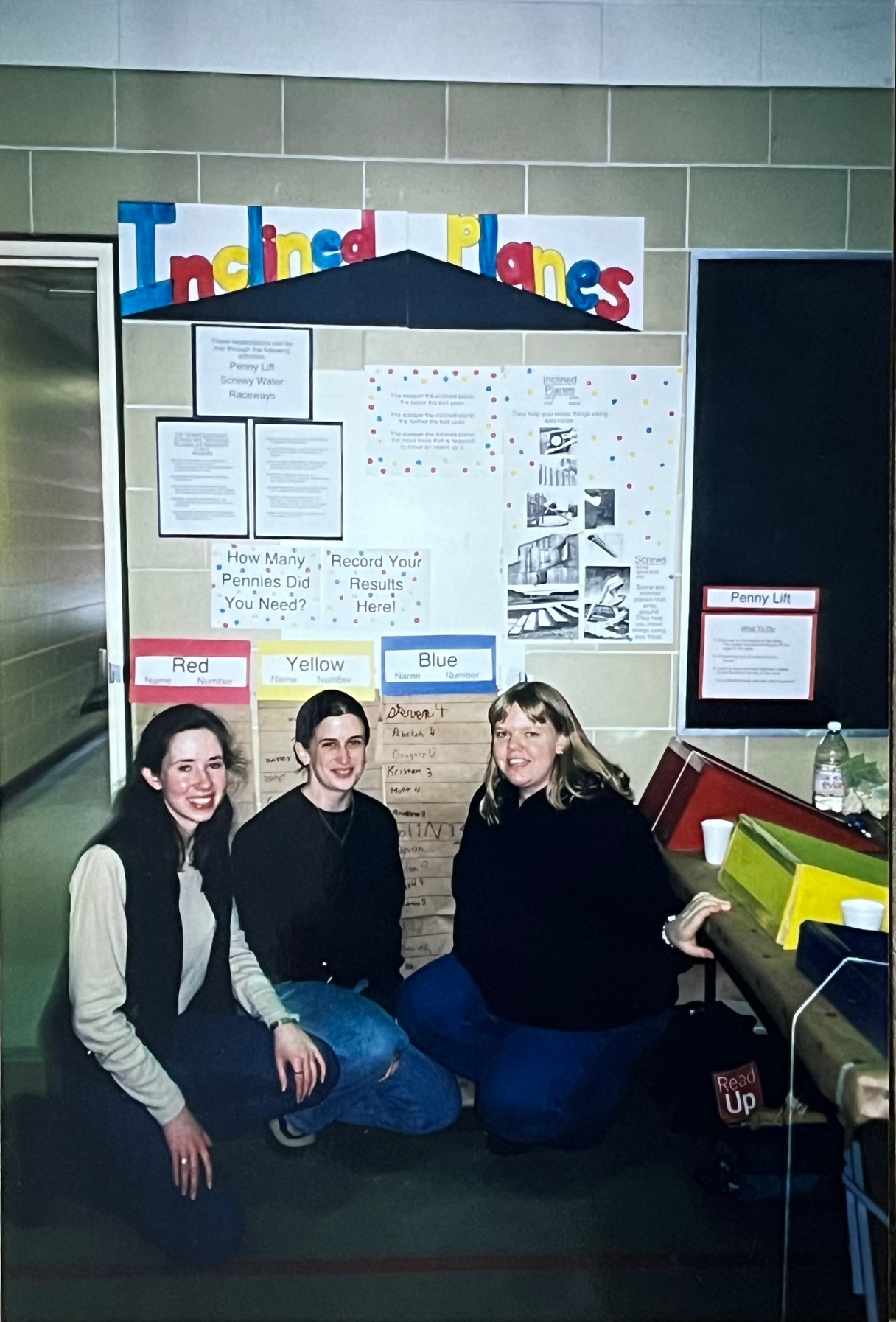 Three students crouch and smile in front of a poster board presentation.