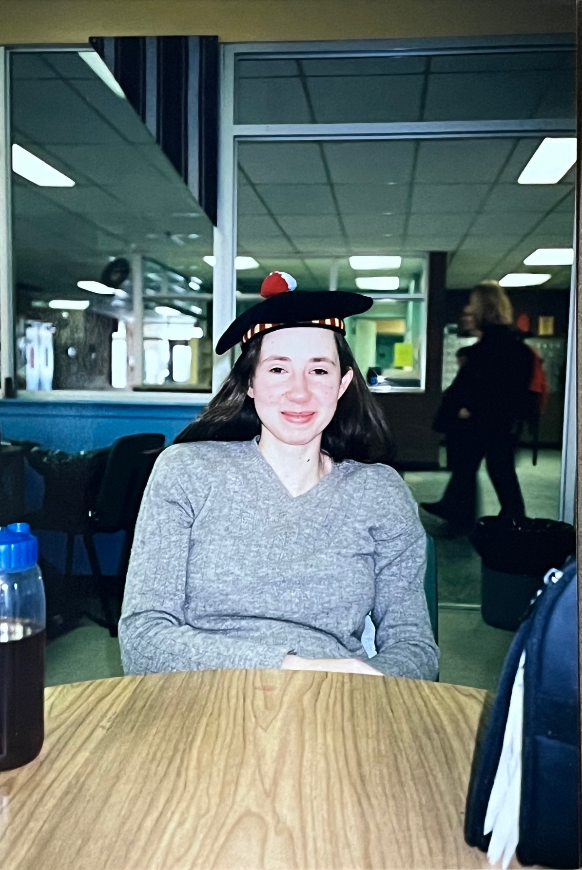 A student poses sitting at a table wearing a Queen's tam.