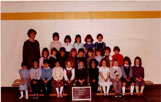 Maureen Watkin in a school photo standing to the left of her class who sit on the bleachers.