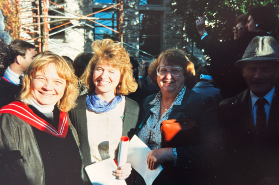 Megan Aston and parents and a friend pose in a film photo at graduation outside of a stone building.