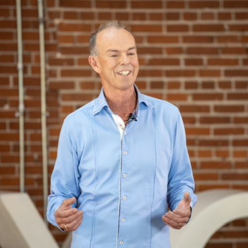 Michael Kehler wearing a blue button down shirt smiling in a red brick room.