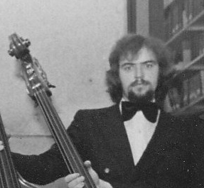Roger Finlay in a bow tie and suit holding the neck of a cello.