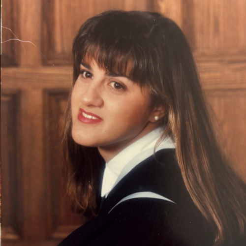 Rose Heron in her grad photo from 1992 wearing graduation robes and posing in front of a wooden background.