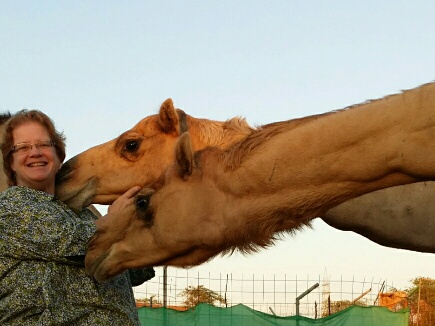 Sheri Henderson smiles while two camels lean their necks towards her.