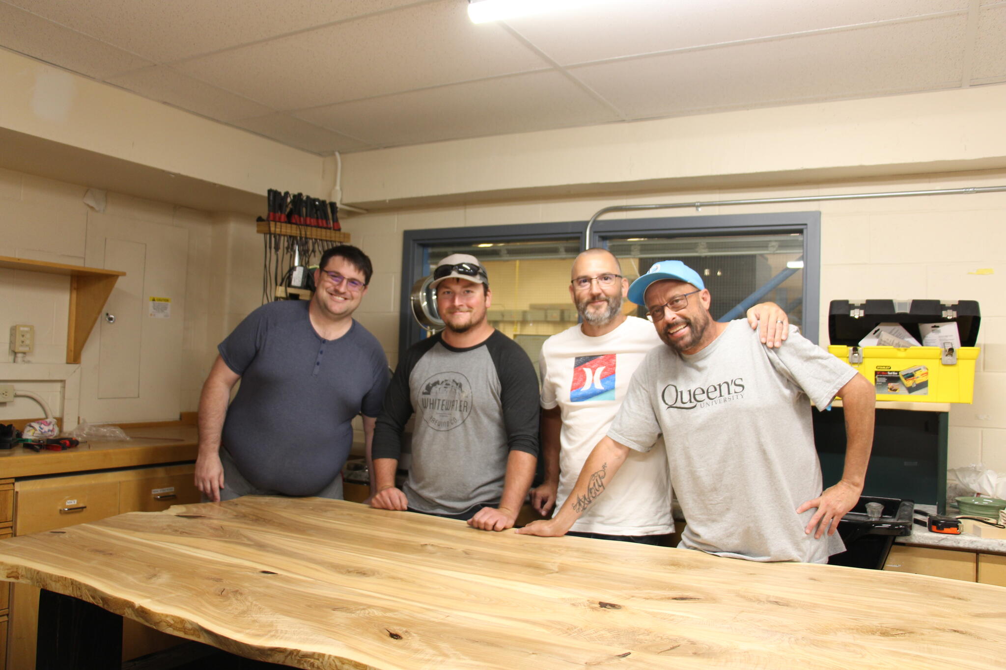 Four tech students stand behind a woodern table in a tech shop.