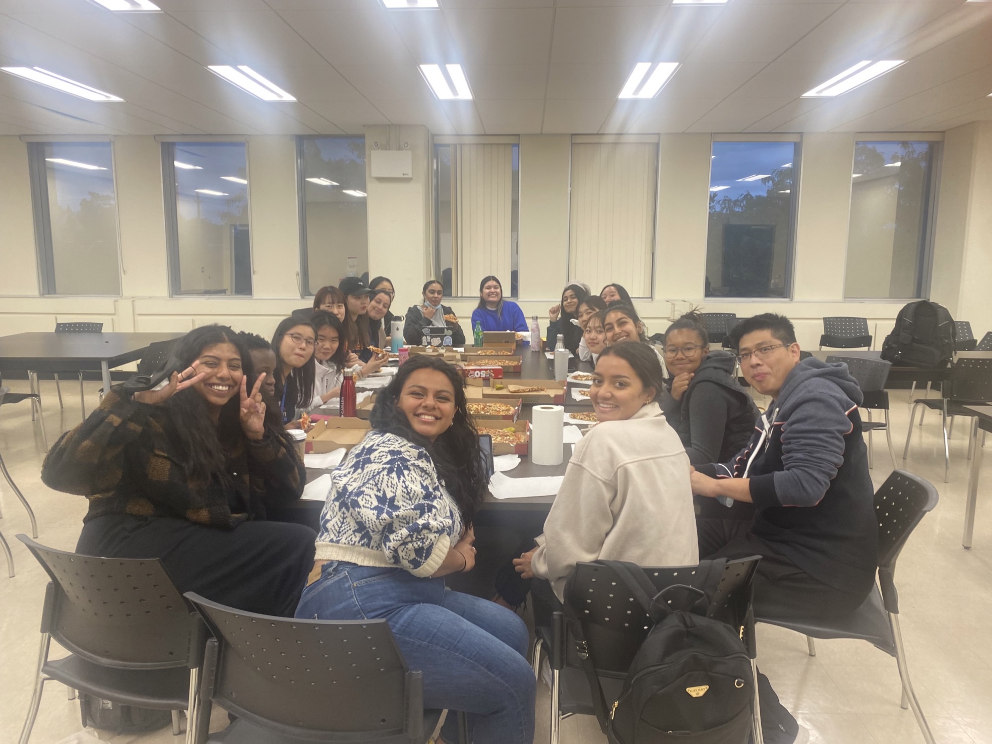 Group photo of the 2022-23 Teacher Candidates of Colour eating pizza around a table.