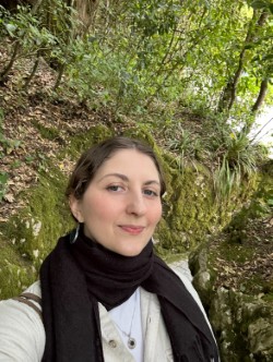 Laura Kelly smiles outside in nature wearing a scarf and a white shirt.