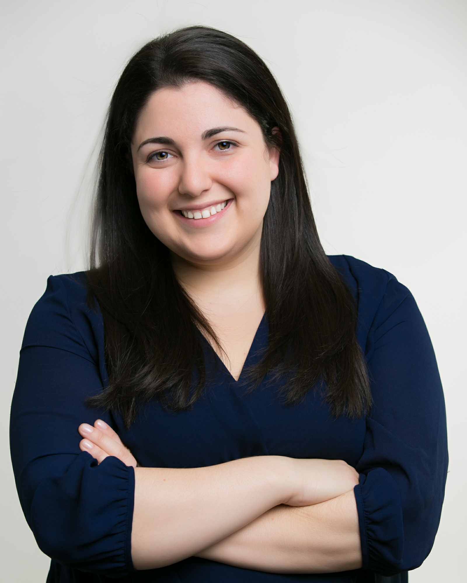 A woman with dark hair poses in front of a white background