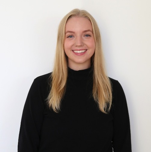 A blond woman with a nose ring in front of a white wall