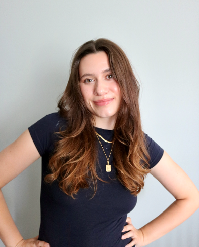 A woman with long brown hair wearing a black tshirt with hands on her hips 