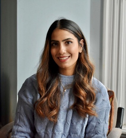 A woman with dark hair smiles wearing a blue sweater