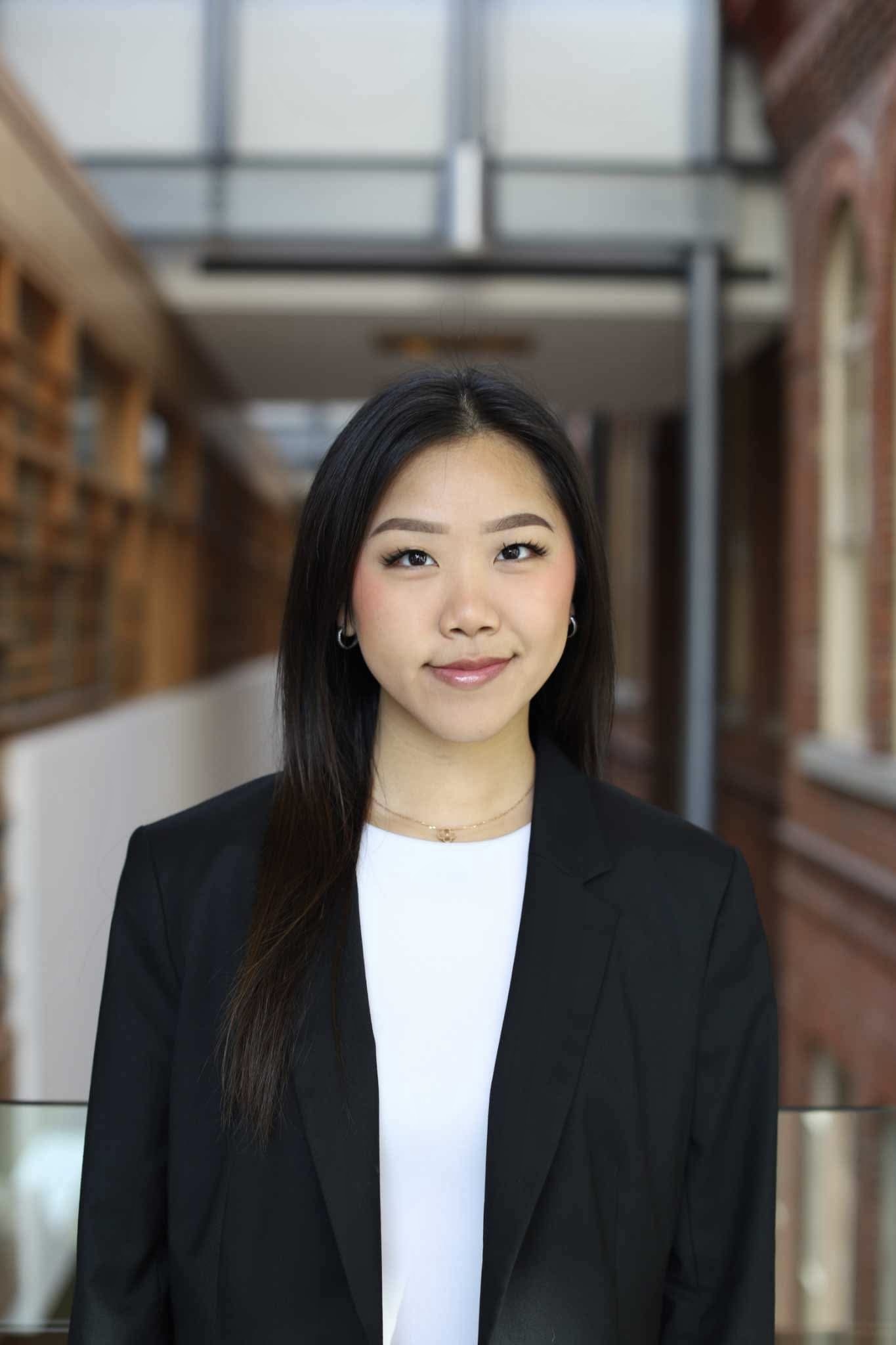 An asian woman wearing a black blazer and a white shirt smiles at the camera 