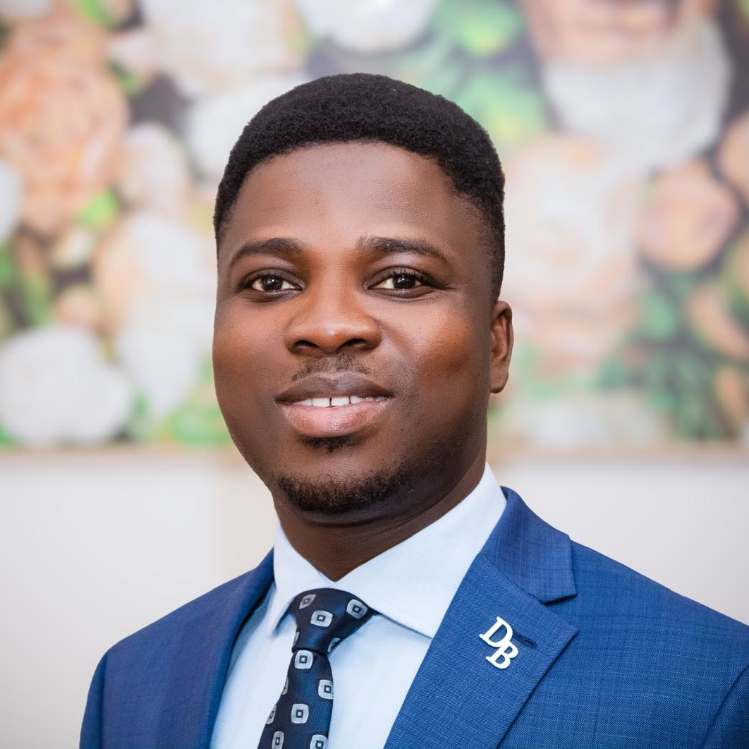 A black man wearing a suit and tie smiles at the camera
