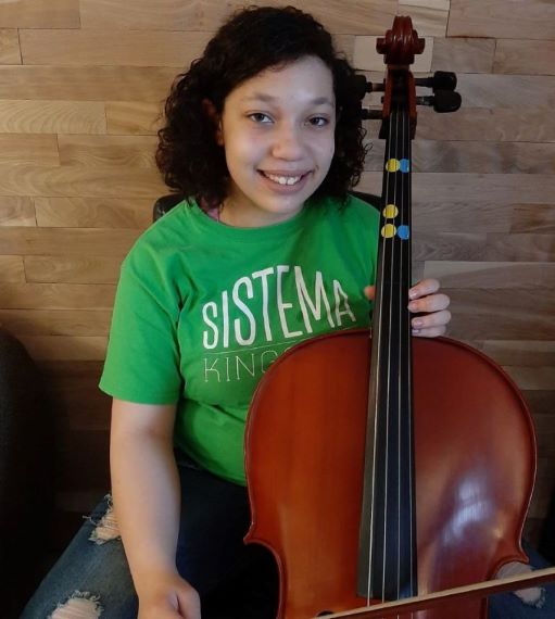 A girl in a green shirt sits holding a cello