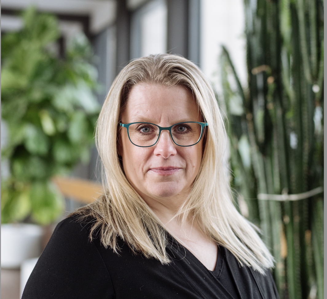 A white woman with glasses and blond hair looks directly into the camera