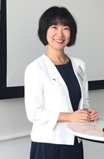 Jia stands at a table wearing a white blazer