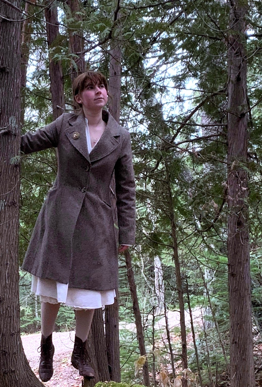 An image of a woman hovering next to a tree in an vintage overcoat