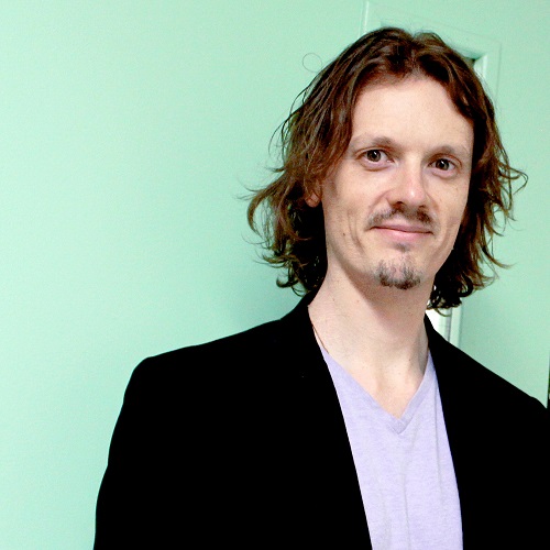 Scott Maybee smiles against a turquoise background.