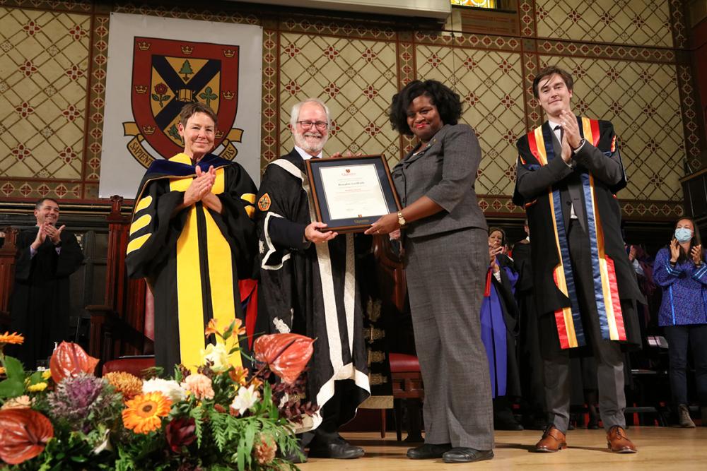 Rosalie Griffith smiles as she receives a framed award on stage at a graduation ceremony.