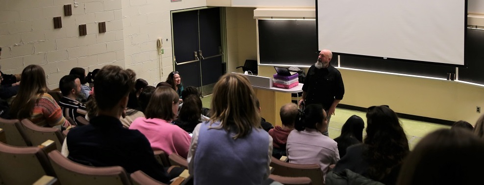 Craig Morrison stands at the front of a lecture hall speaking to a group of students.