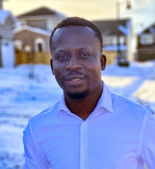 Kenneth Gyamerah smiles outside wearing a white collared shirt in a snowy background.