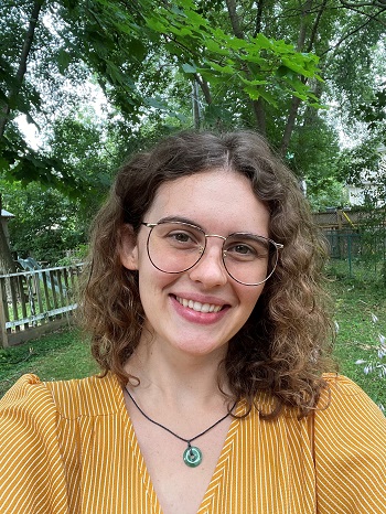 Emily Duncan smiles outside. She wears glasses and a yellow shirt.