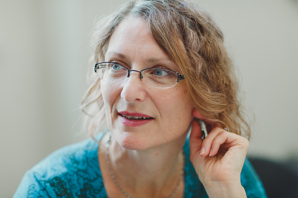 Patty Douglas looks to the left side of the camera wearing glasses and a blue shirt