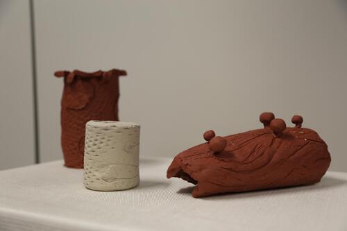 Three clay artworks sit on a plinth. Two are terracotta clay and one is small white clay cup.