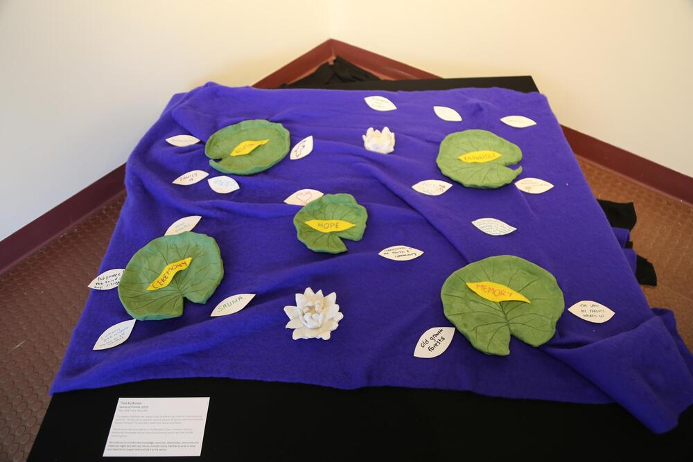 A large piece of blue felt sits on a raised platform with felted lillies and lily pads. Small pieces of paper are nestled among the felt.