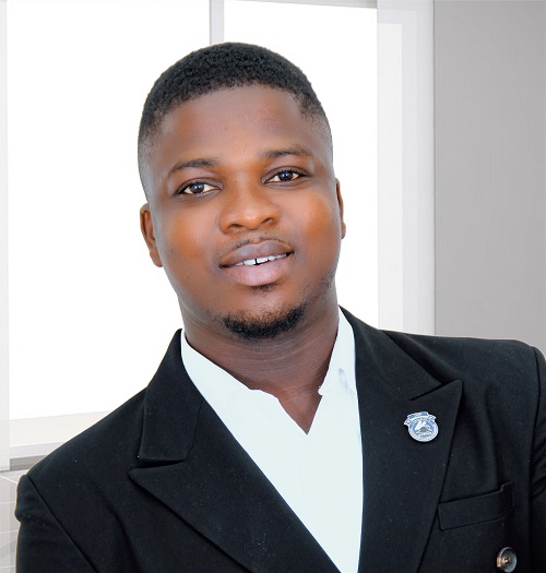 David Baidoo-Anu poses in a suit jacket in front of a window.