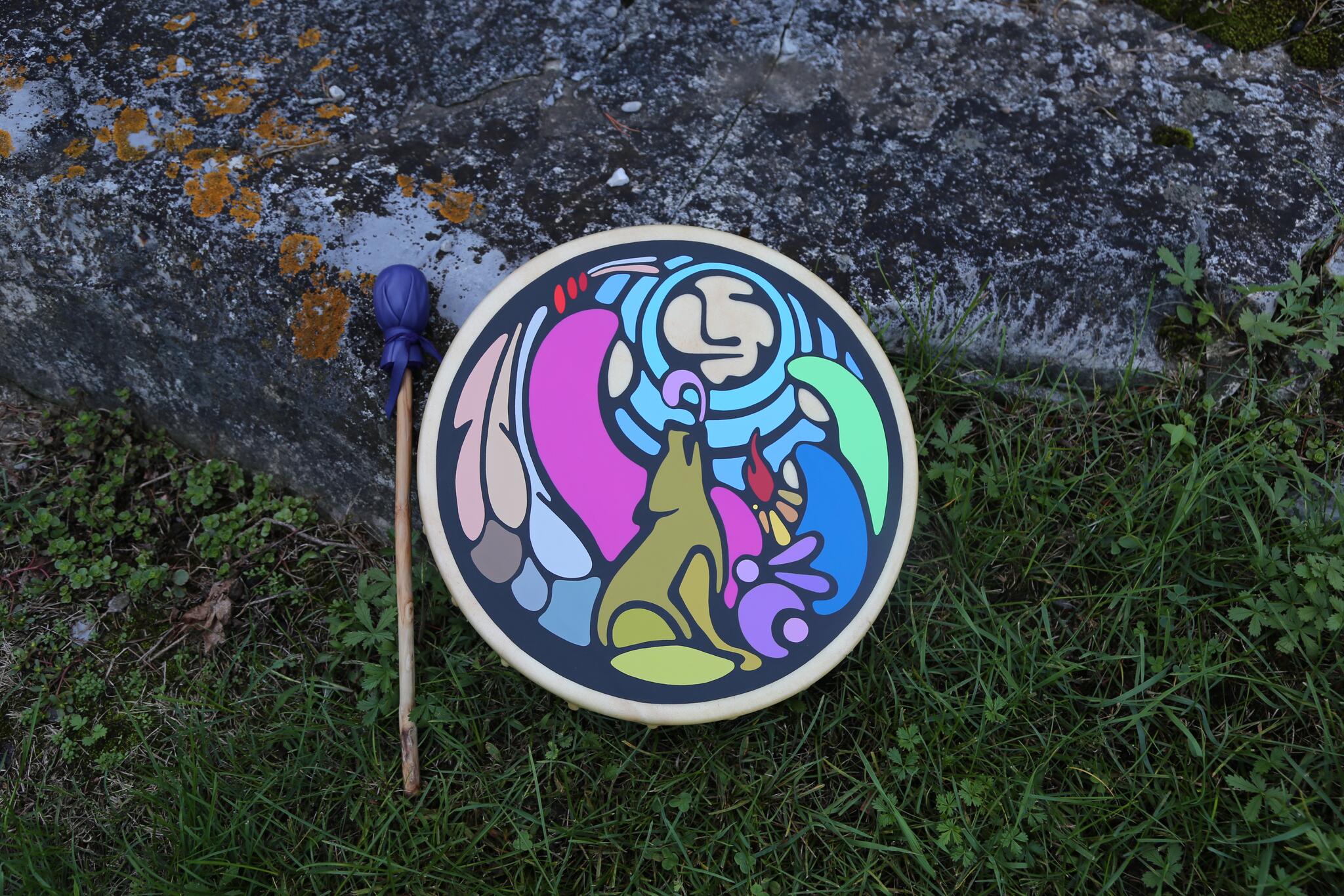 A colourful painted hand drum rests against some grass and rocks.