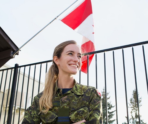 Elyse O'Brien wears a camouflage uniform and stands in front of a Canadian flag.