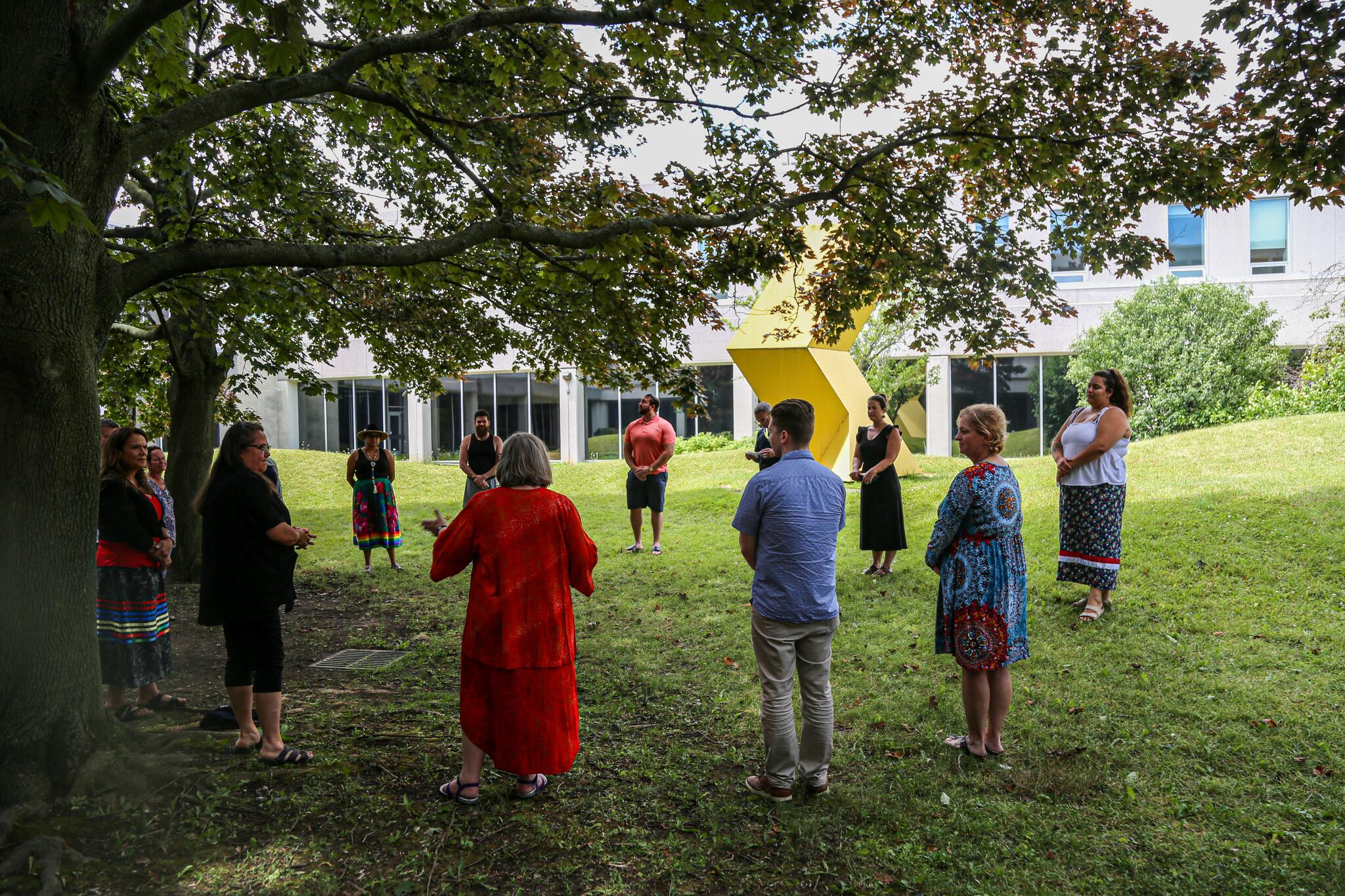 Students stand in a circle outside under some trees.