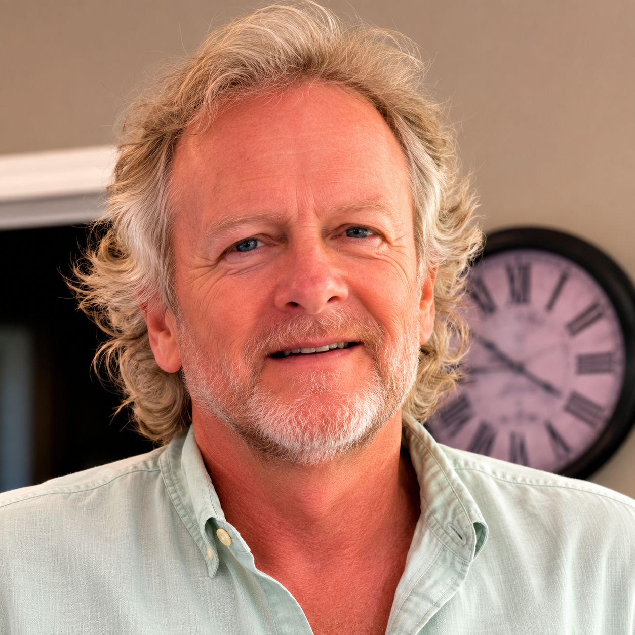 A man smiling at a camera wearing a blue button up