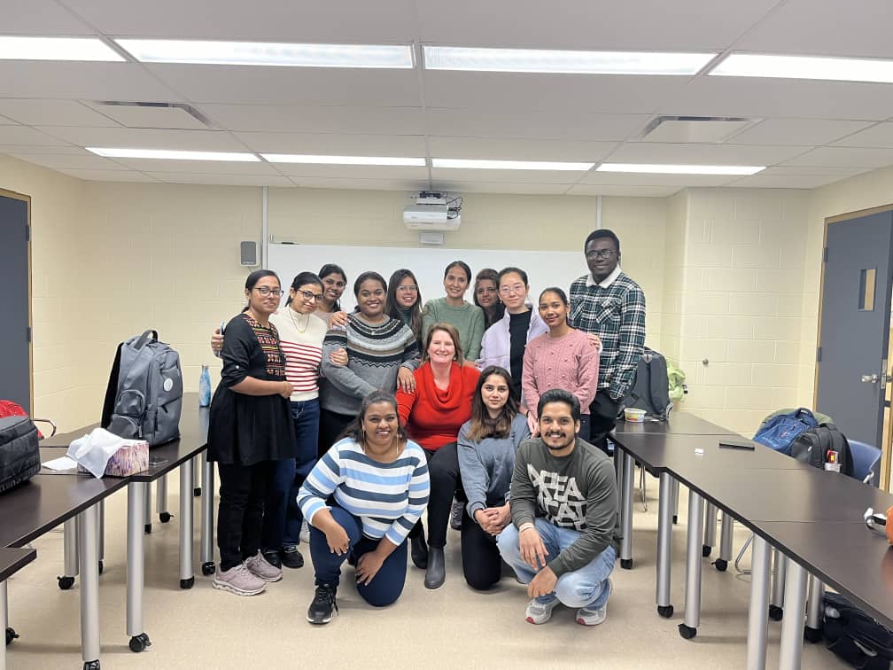 A group of adult students in a classroom smile at the camera 