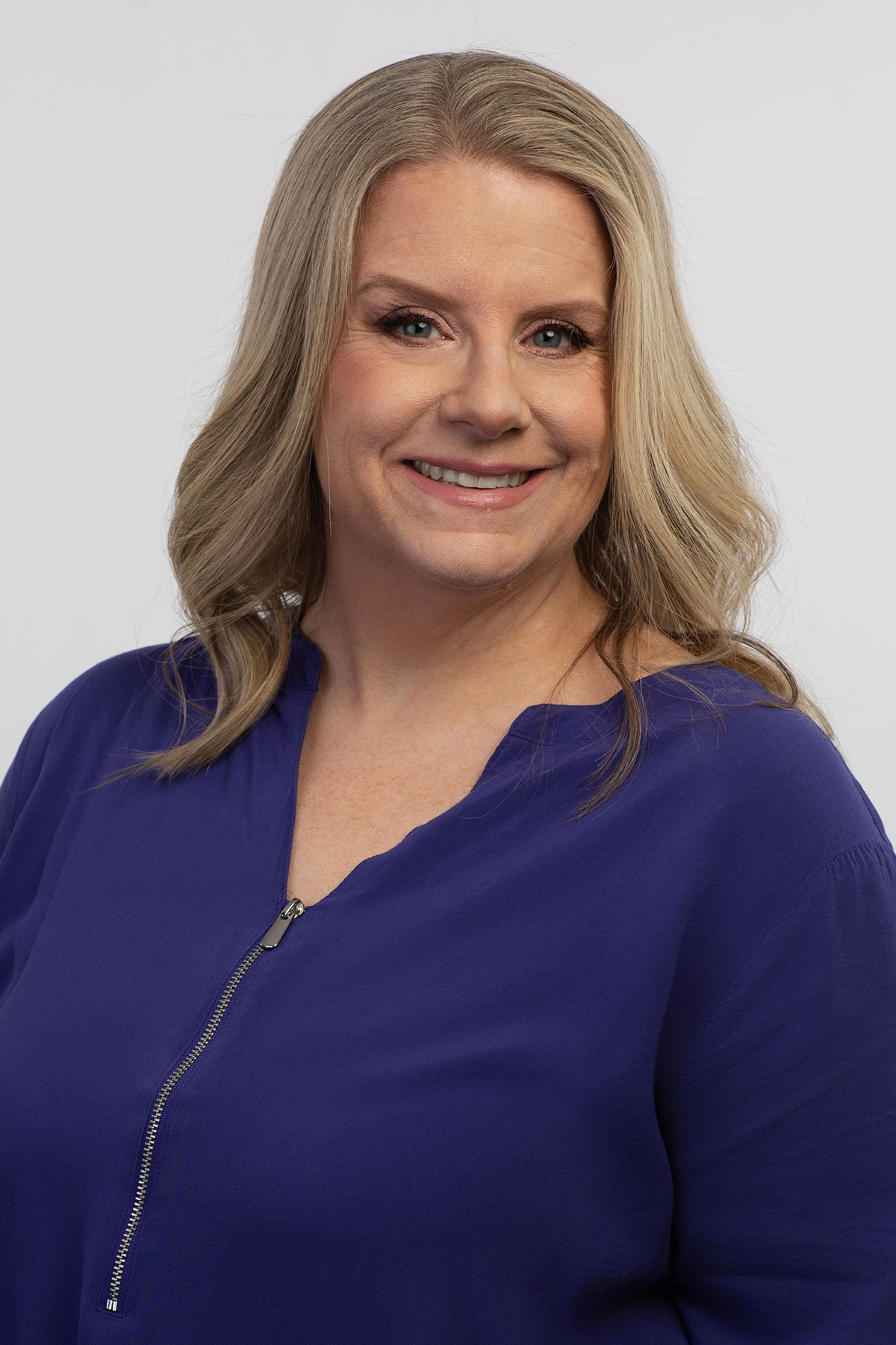 A white woman with blond hair smiles while looking at the camera