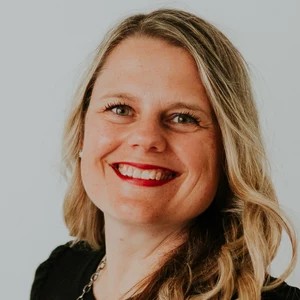 A white woman with blond hair smiles while looking at the camera