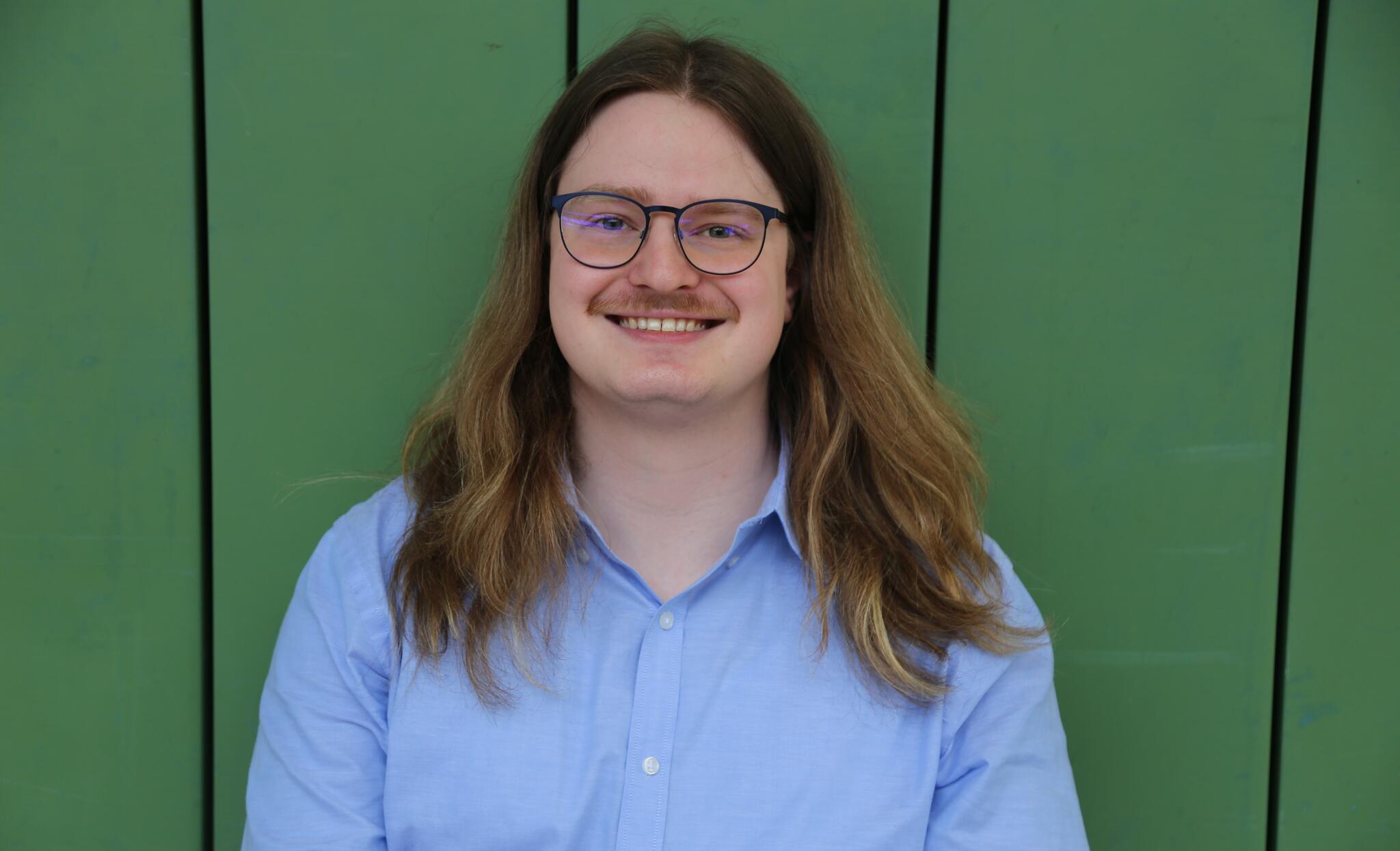 A white man with long hair and glasses smiles at the camera 