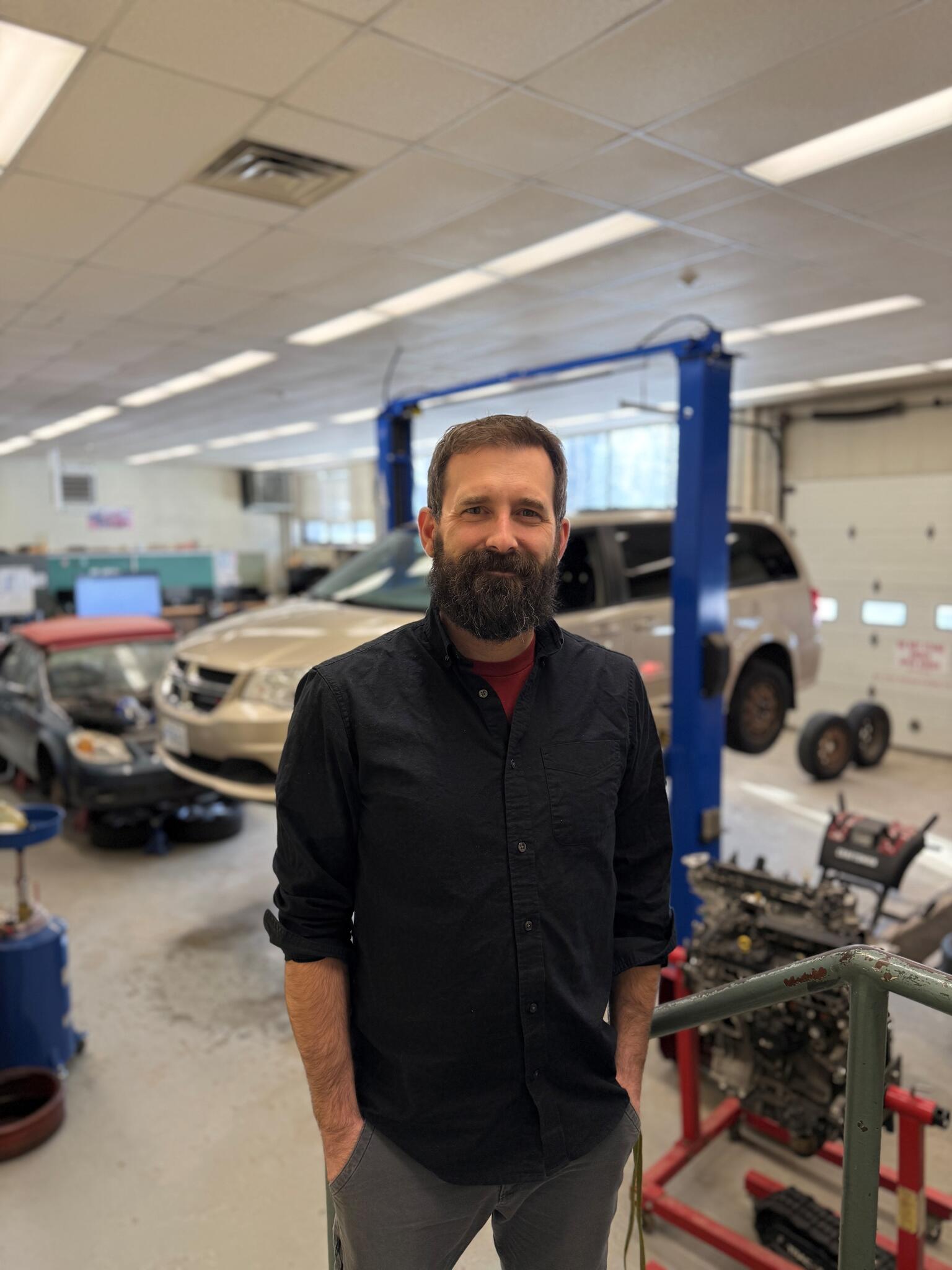 A man smiling in front of a car shop