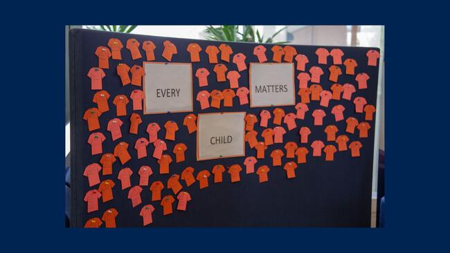 A board with orange paper t shirts on it, it reads "Every Child Matters."