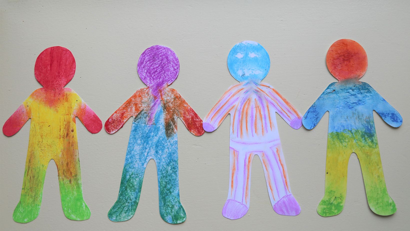 Four paper dolls coloured in with pastels.
