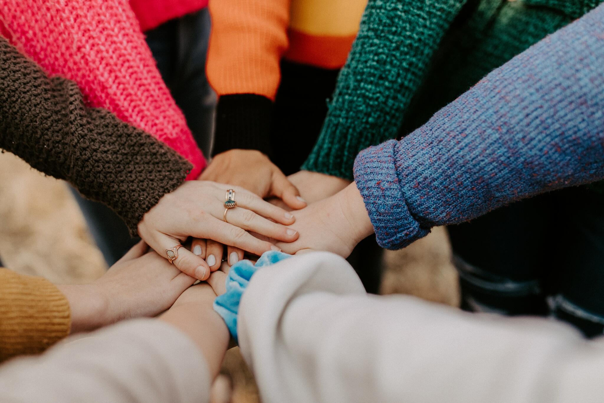 Many different people put their hands on top of each other's hands in a circle.